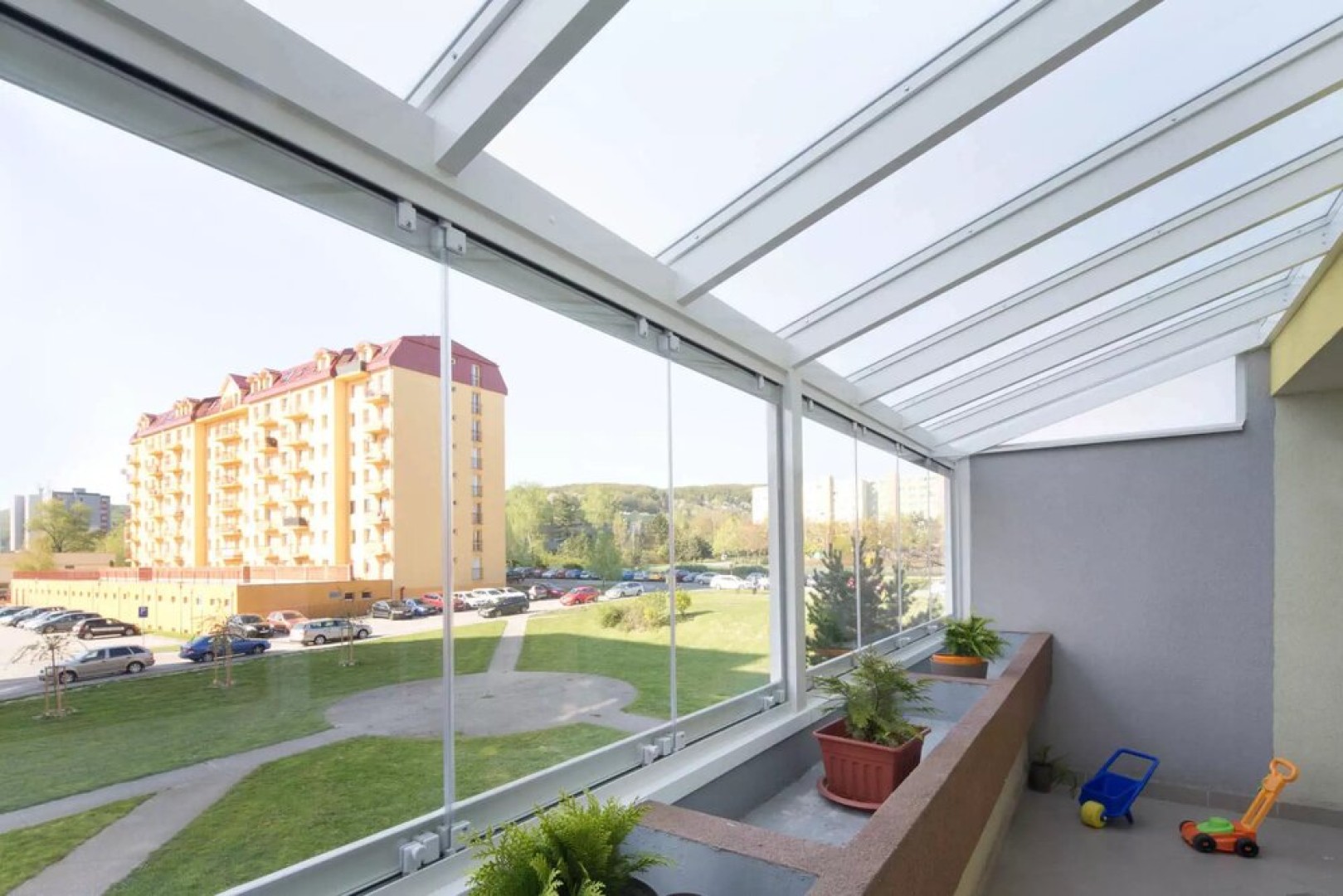 Modern frameless balcony glazing with a view of the housing development and greenery