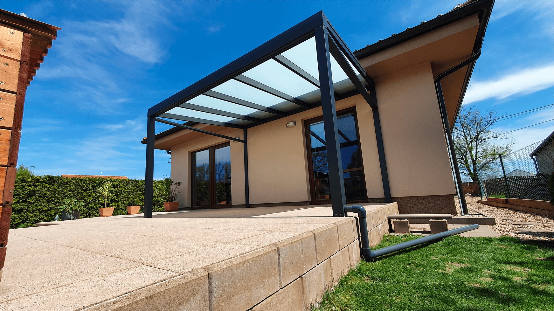 A modern anthracite-colored aluminum pergola with a glass roof on the terrace of a single-family home