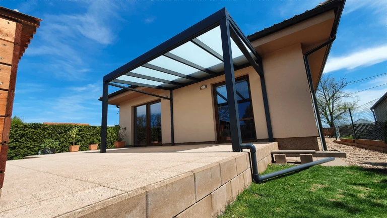 A modern anthracite-colored aluminum pergola with a glass roof on the terrace of a single-family home