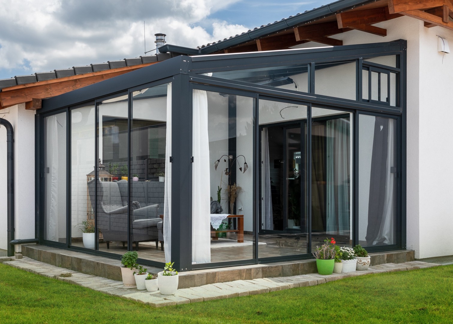 A modern glass addition to a single-family home with a gray aluminum frame and sliding doors.