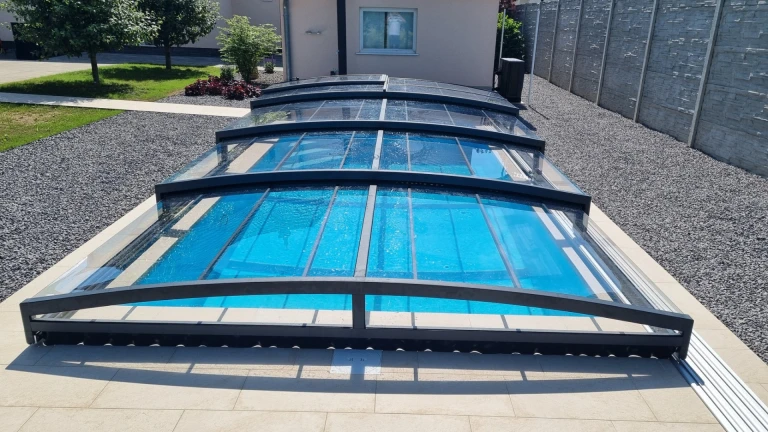 A modern, low-profile pool enclosure with a transparent panel in the garden