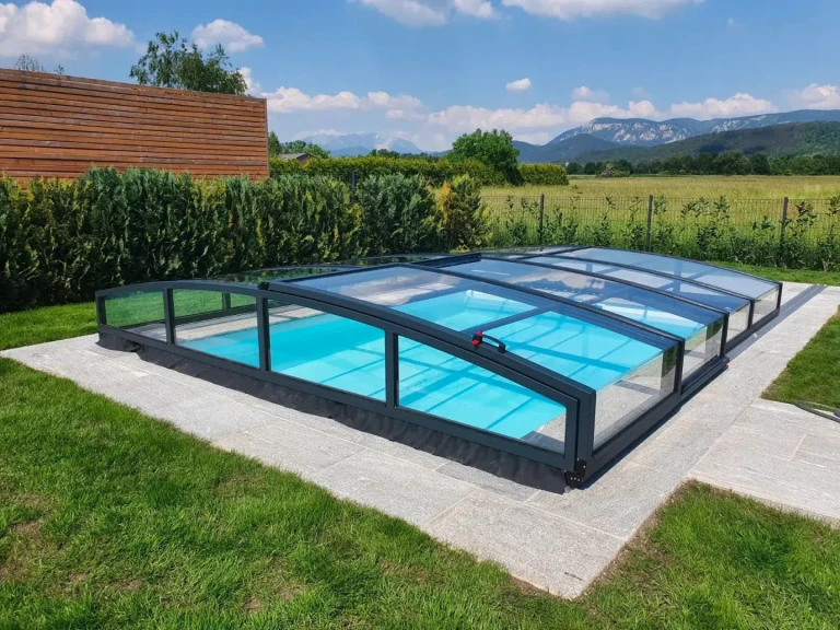 A modern, low-profile STAR pool enclosure in anthracite, set in a garden with a view of the mountains