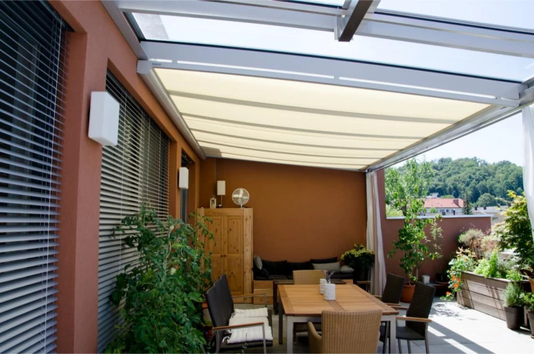 A modern patio with a dining area under a retractable fabric awning and a glass roof.