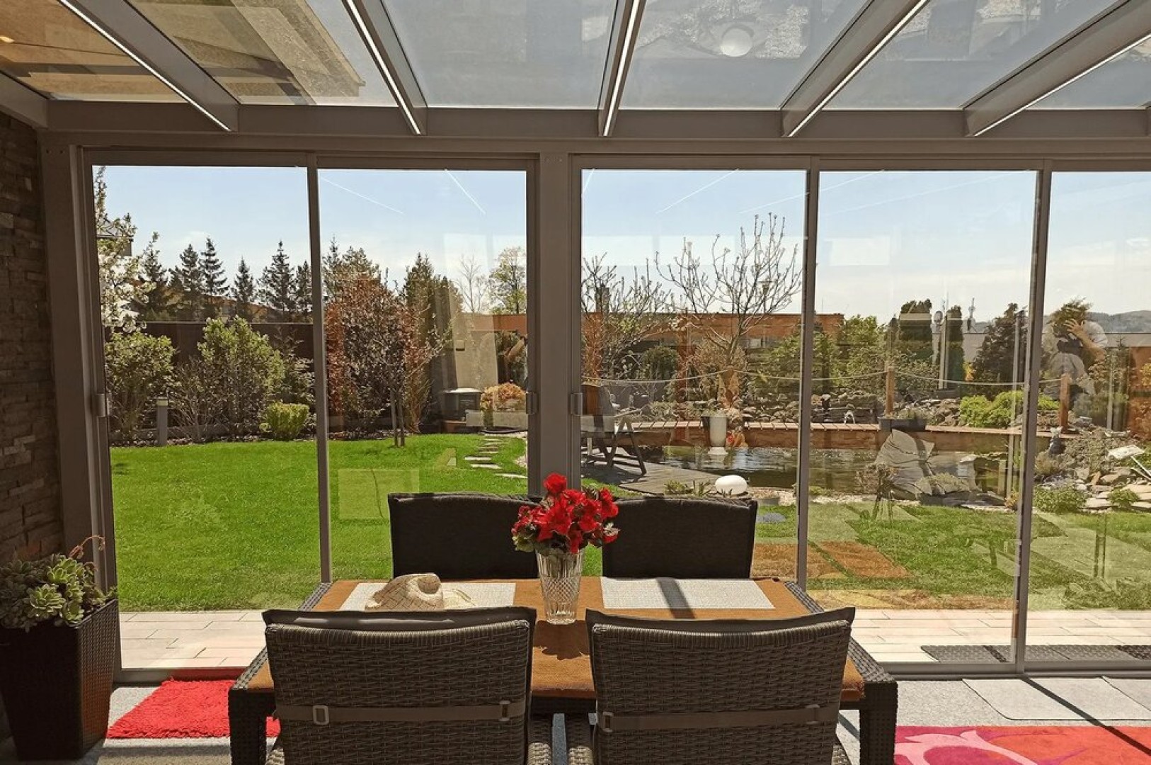 A glass-enclosed terrace overlooking the garden, with seating and flowers