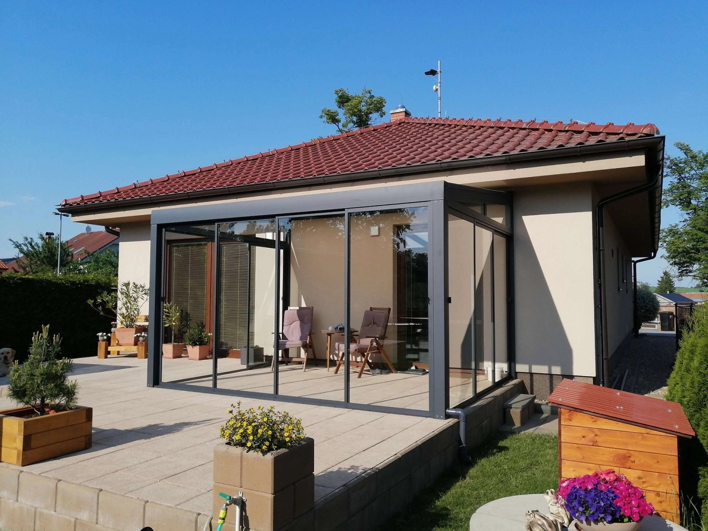 A modern, glass-enclosed sunroom with an anthracite-colored frame on the terrace of a single-family home