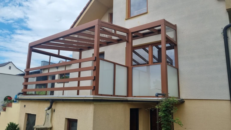 A modern brown aluminum pergola with glass panels on the terrace of a single-family home.
