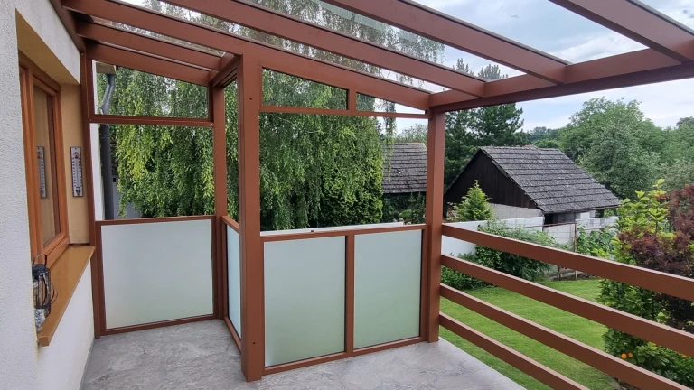 A side view of a brown aluminum pergola with a glass roof and frosted panels on the patio.
