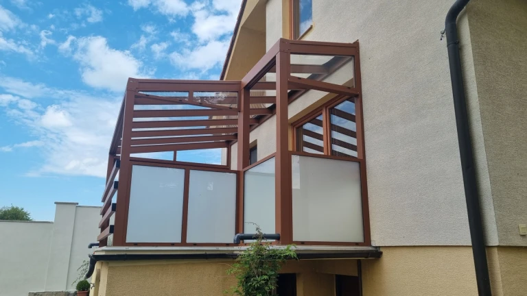 A brown, custom-designed aluminum pergola with safety glass installed on the balcony of a single-family home.