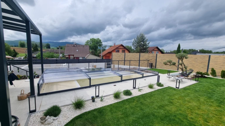 A modern, low-profile pool enclosure in the garden of a single-family home with a view of the hills.