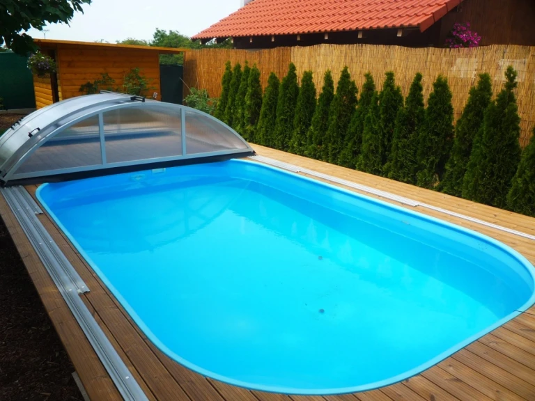 A blue pool with wooden paneling and a partially open sliding cover in the garden.