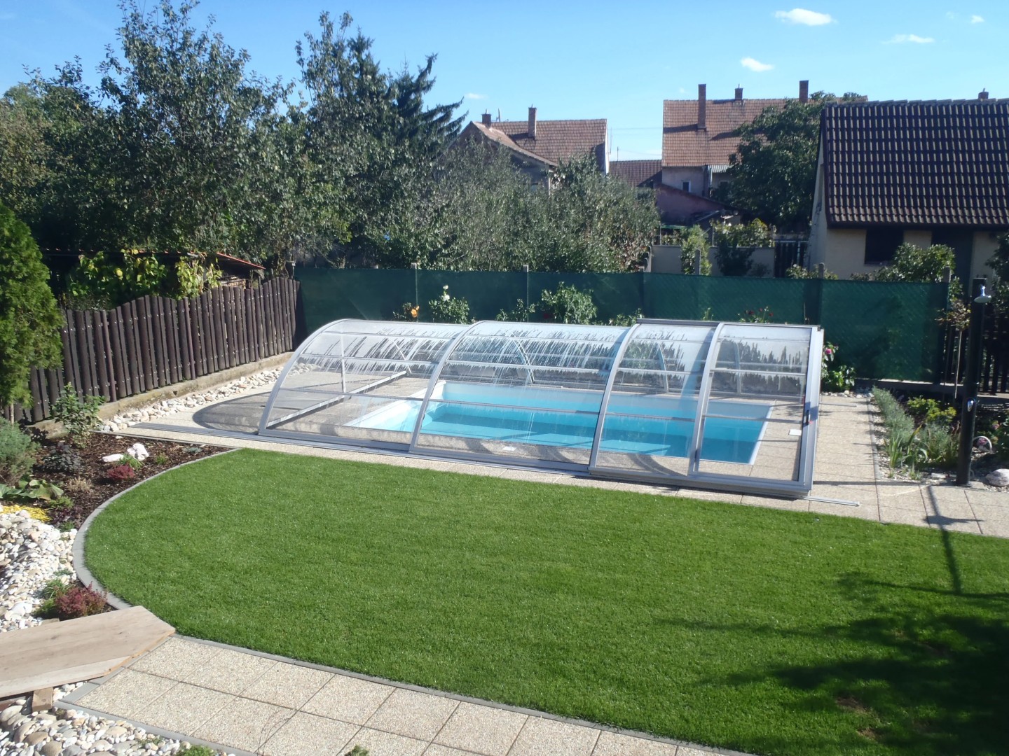 A modern, low-profile pool enclosure in the garden of a single-family home with a lawn.