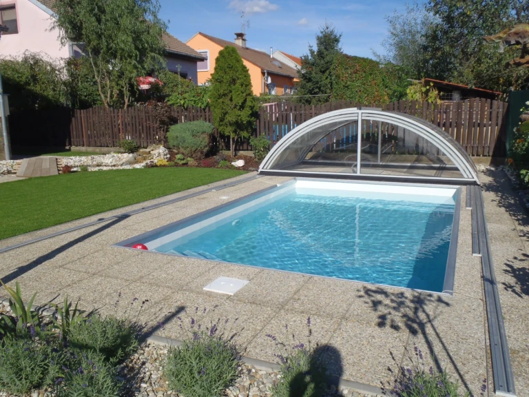 A modern swimming pool with a partially retractable sliding roof in the garden of a single-family home.