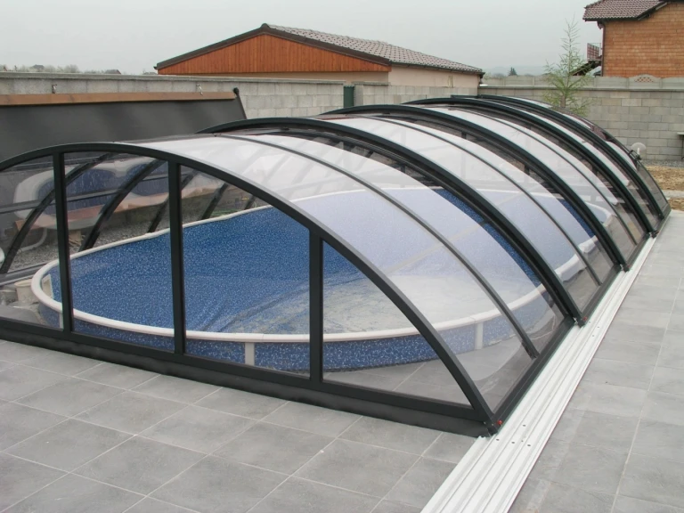 An arched pool canopy with a gray frame and clear panels over an oval pool.