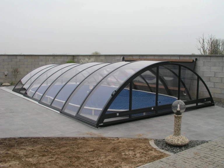 A low, anthracite-colored pool enclosure with a rounded profile on a paved terrace