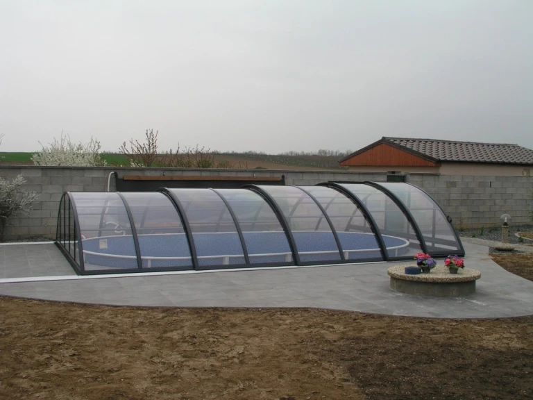 A KLASIK enclosed pool enclosure with dark profiles on a paved patio in the garden.
