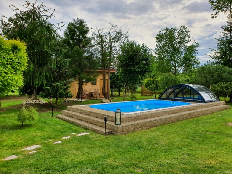 A backyard pool with a blue liner and a low-profile sliding cover on a raised deck surrounded by greenery.