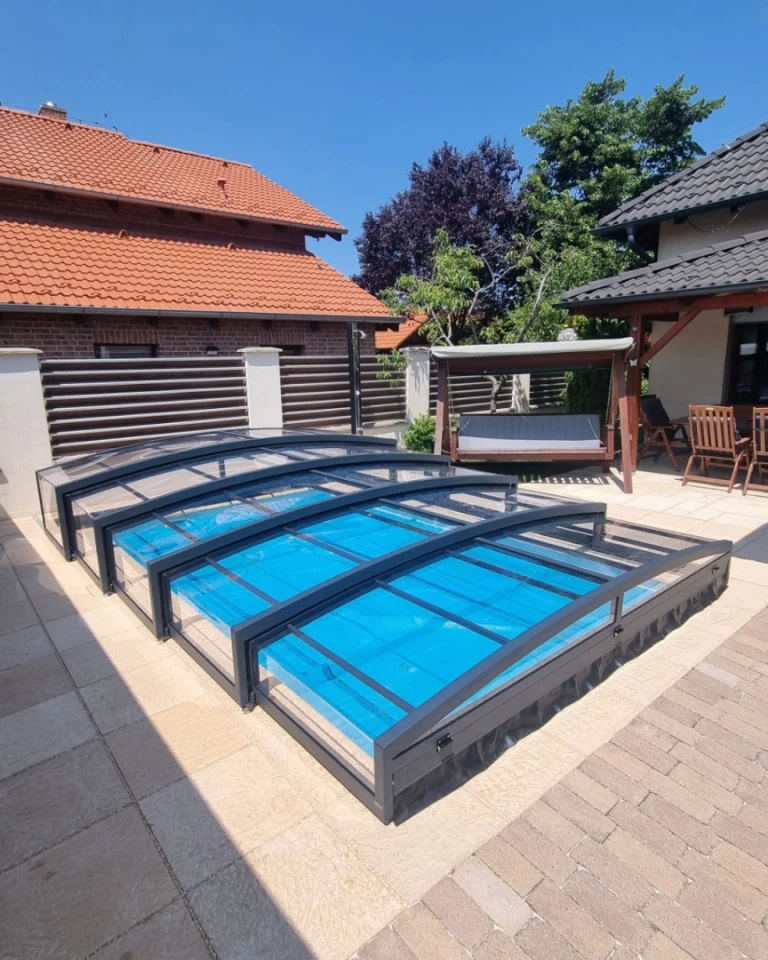 A low, anthracite-colored telescopic pool enclosure on the paved area in the garden of a single-family home.