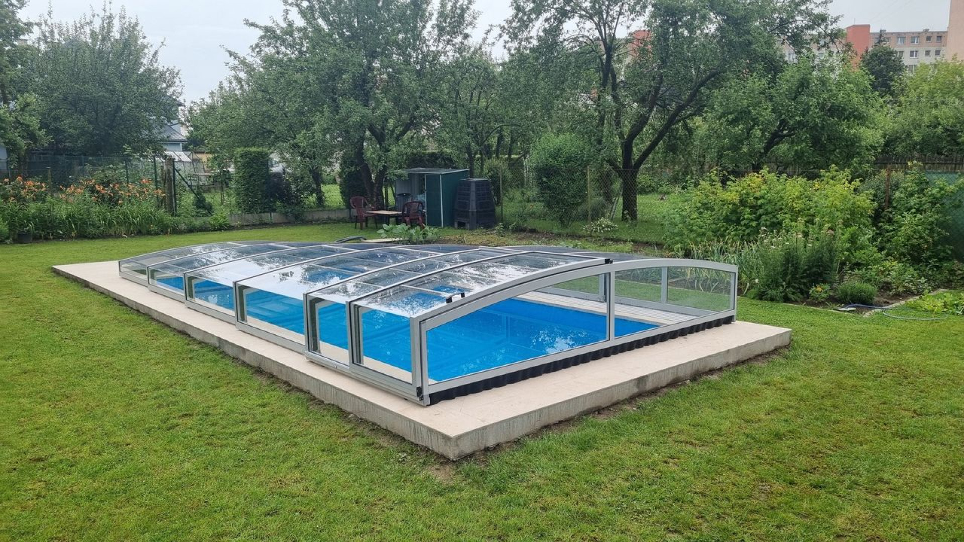 A low-profile PREMIER pool enclosure over a blue pool in a garden in Martin.