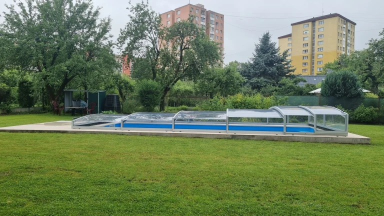 A low-profile PREMIER pool enclosure in a garden in Martin, with a green lawn and apartment buildings in the background