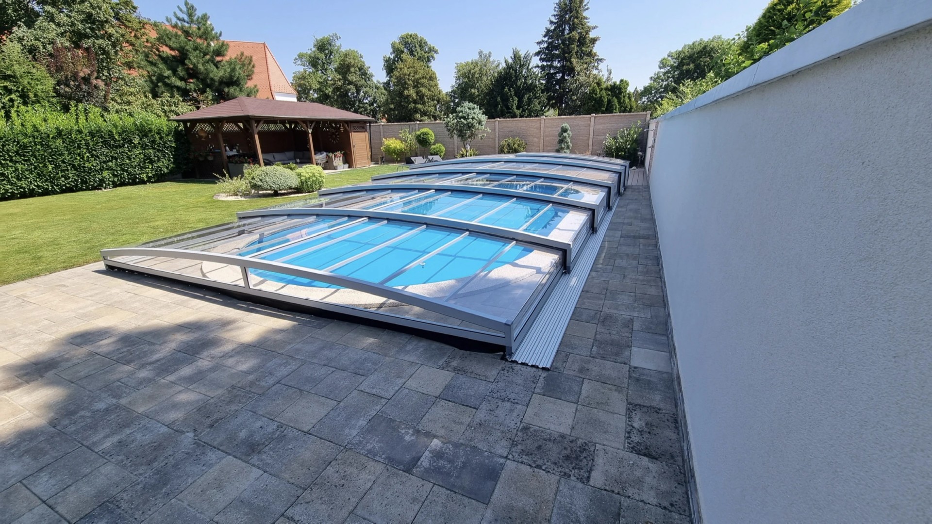 A modern, low-profile PREMIER pool enclosure with a transparent panel in a garden in Modra