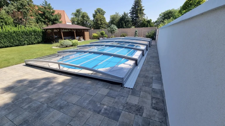 A modern, low-profile PREMIER pool enclosure with a transparent panel in a garden in Modra