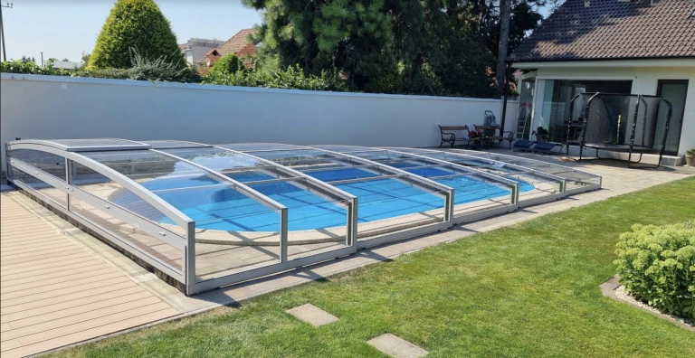 A modern, low-profile pool enclosure with a transparent panel in the garden of a single-family home