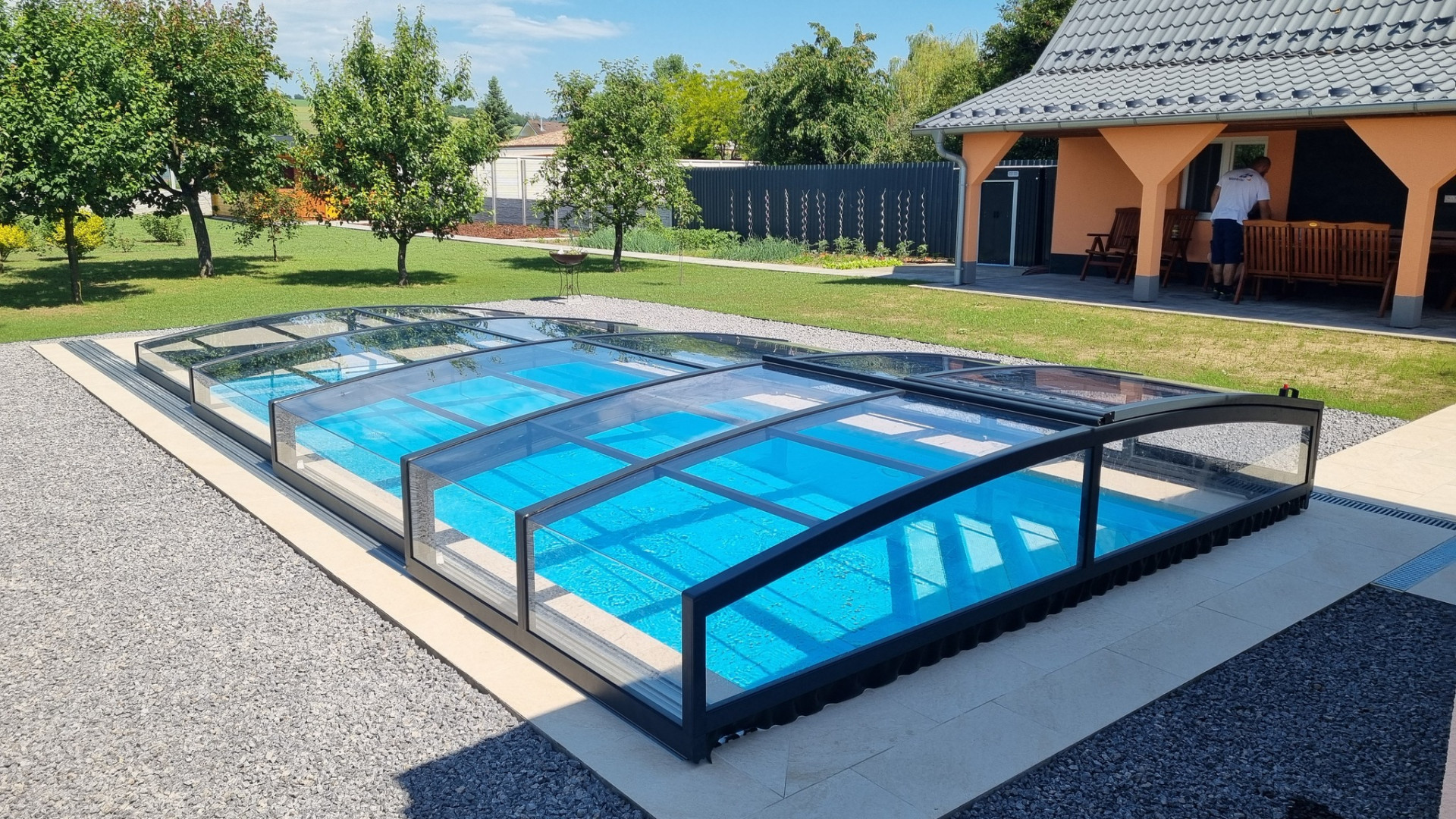 A modern, low-profile PREMIER pool enclosure with a dark frame in the backyard of a single-family home.