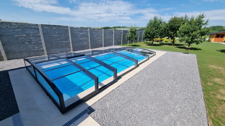 A modern, low-profile PREMIER pool cover with a dark frame in the garden next to a concrete fence