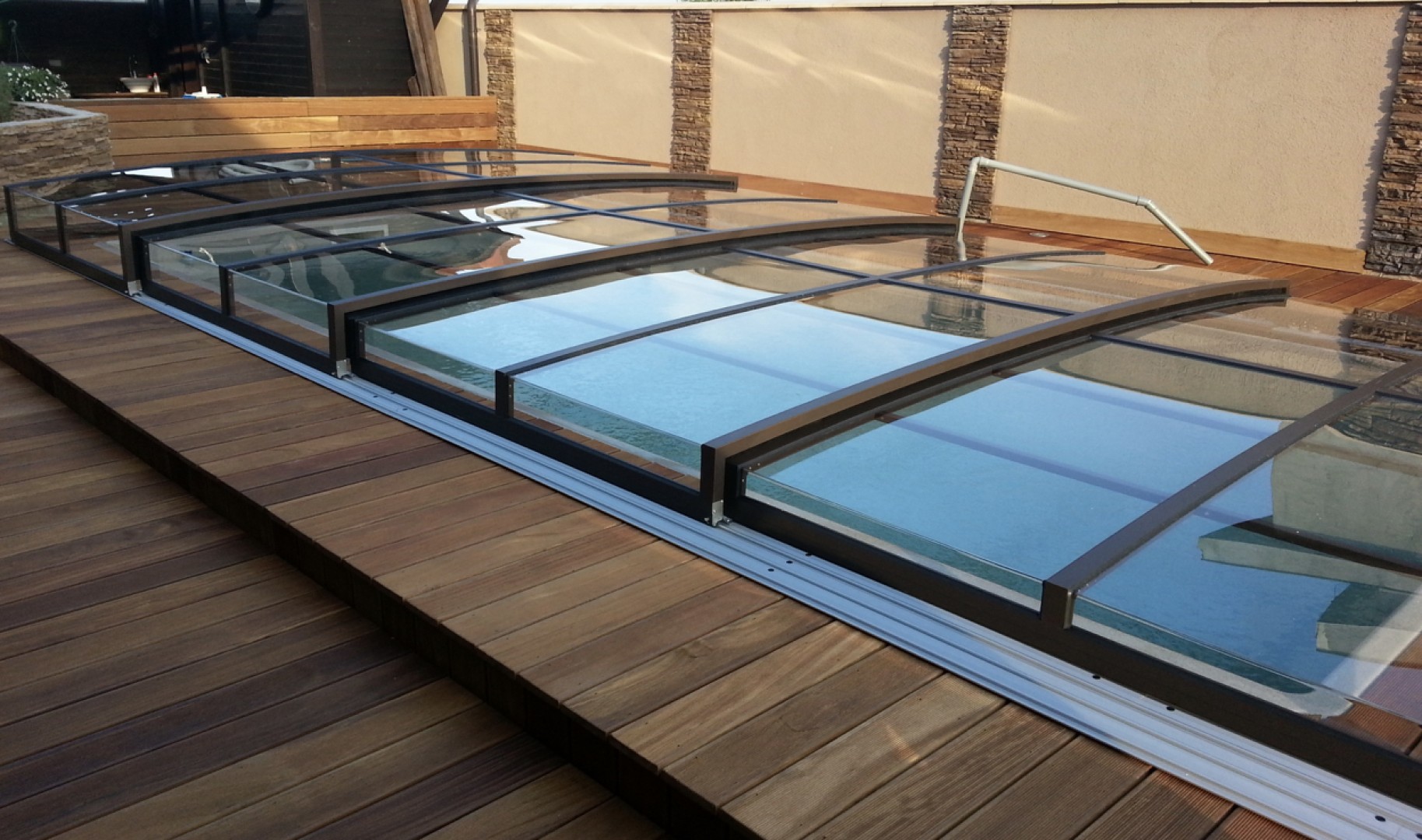 A modern, low-profile STAR pool enclosure in a dark color on a wooden deck