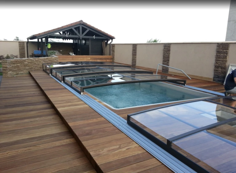 A modern, low-profile pool enclosure with sliding glass panels on the wooden deck of a single-family home.