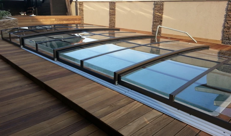 A low anthracite-colored pool enclosure with clear panels, installed on a wooden deck