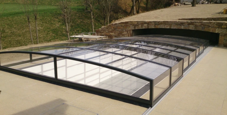A modern, low-profile pool enclosure with a dark frame and clear glass that slides under the deck.