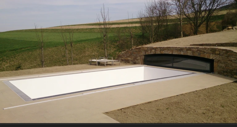 A modern pool with a white cover and a stone wall outdoors, overlooking the hills