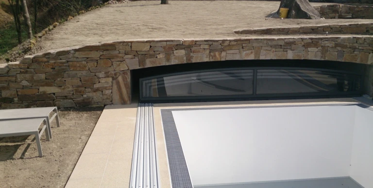 A modern pool enclosure that slides under the stone terrace next to the pool.