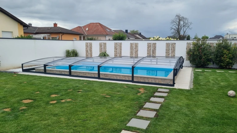 A modern, low-profile pool enclosure in anthracite in a garden with a lawn