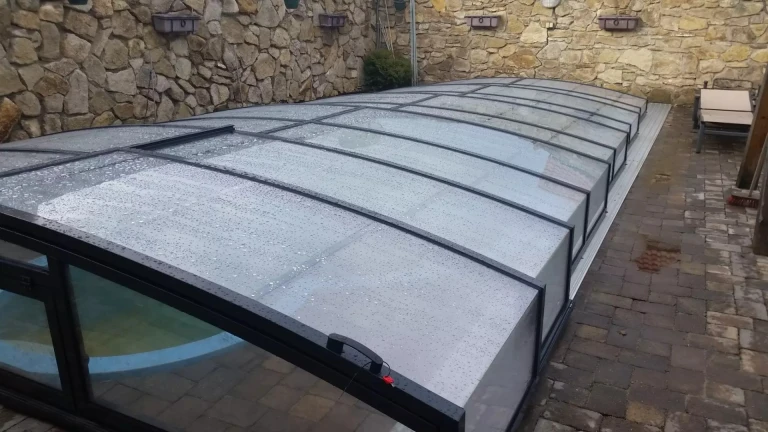 A modern, low-profile pool cover with a black frame and translucent panels in a backyard with stone paving.