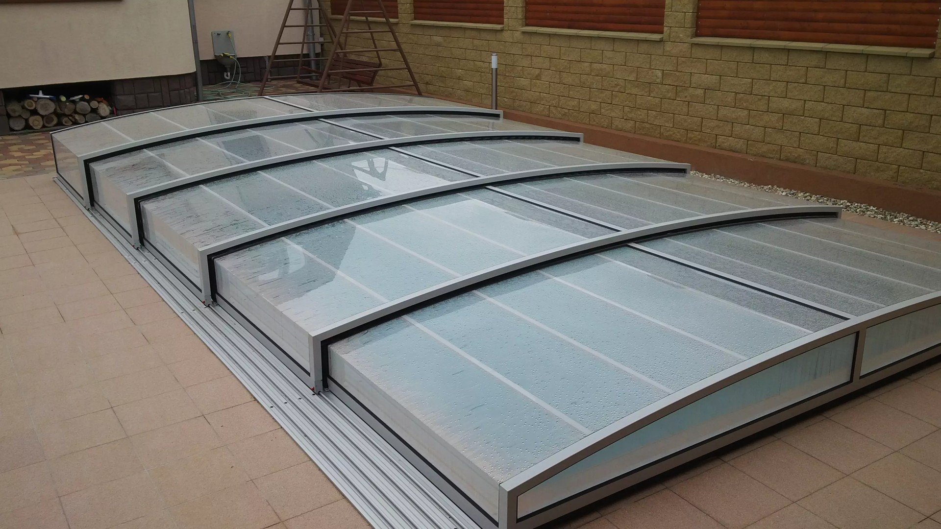 A modern, low-profile pool enclosure with an aluminum frame and clear panels.