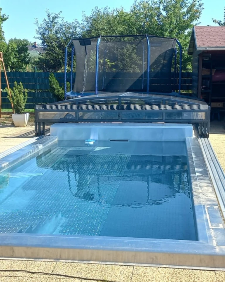 A modern swimming pool with a low, cantilevered roof in a garden featuring a trampoline.