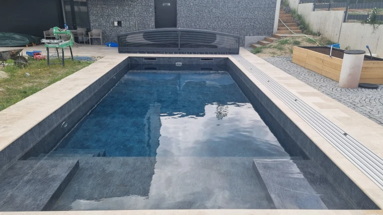 A modern in-ground pool with dark tiling and a low, set-back canopy on the terrace next to the house.