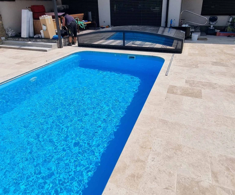 A modern pool with clear blue water and a partially open black canopy on a terrace with stone pavers.