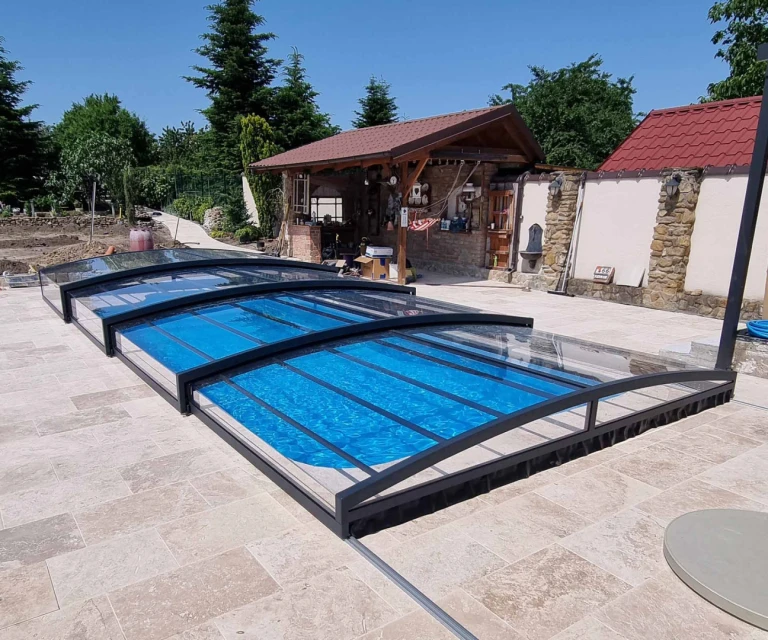A modern, low-profile pool cover with a dark frame and clear panels on a stone patio.