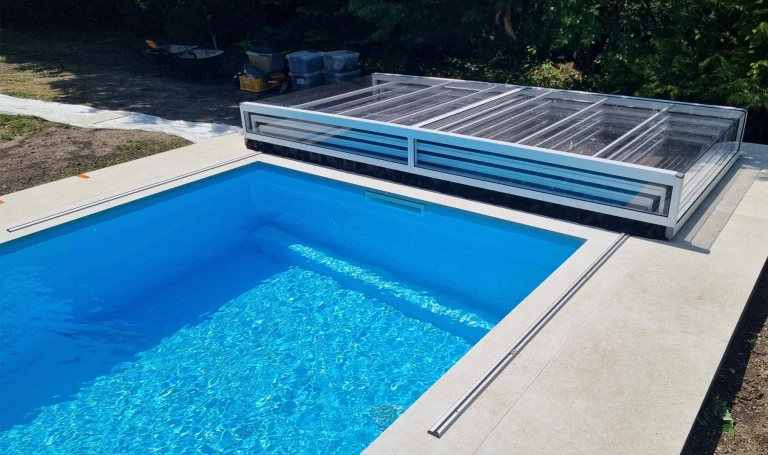 A modern blue pool with a white, trackless EXCLUSIVE cover, folded and placed at the edge of the pool.