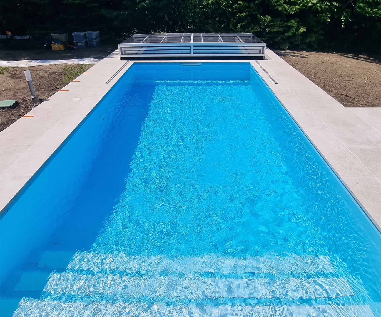 A modern rectangular pool with bright blue water and an elegant white border in the garden.