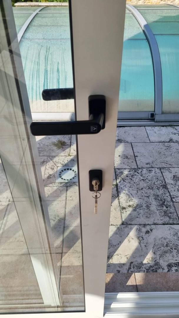 A close-up of a black doorknob and a lock with a key on the white door of the patio enclosure.
