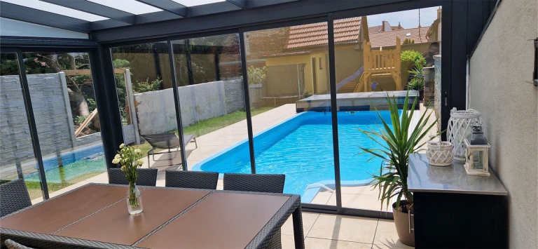 A view from inside the ROBUST maintenance-free sunroom of the pool in the garden, featuring sliding glass walls.