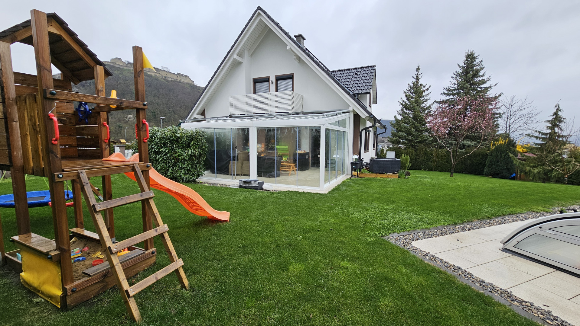 A modern single-family home with a lawn, a playground, and a glass-enclosed addition.
