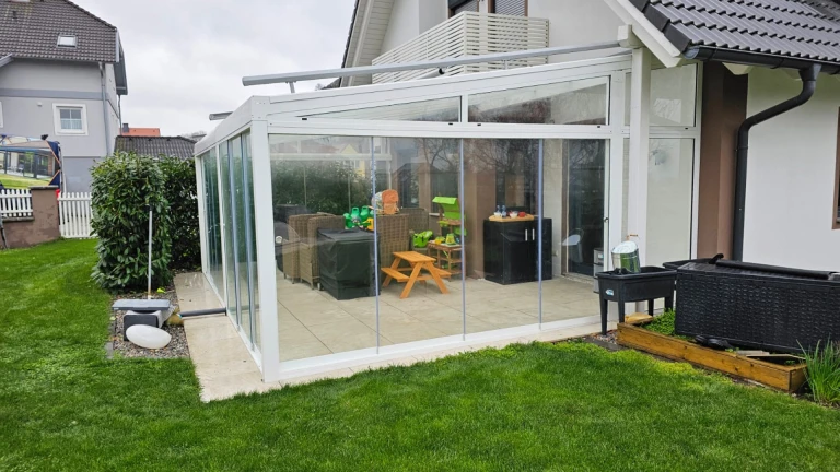 A modern glass addition to a single-family home with garden furniture and toys.