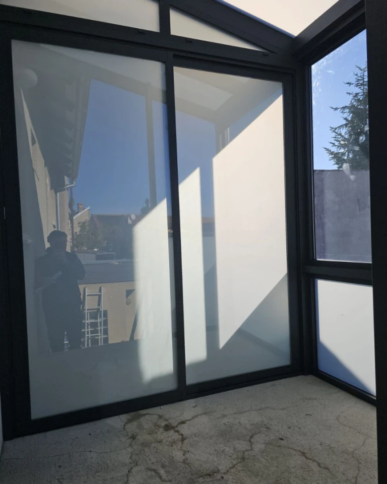 A modern sunroom with a dark aluminum frame and frosted glass at the bottom of the door.