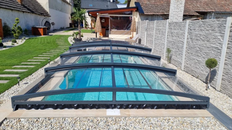 A modern, low-profile pool enclosure with an anthracite frame and clear panels in the garden