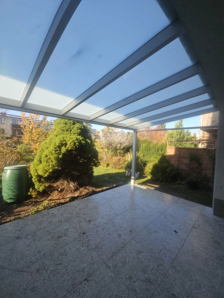 A modern aluminum pergola with a glass roof over the patio, overlooking the garden.